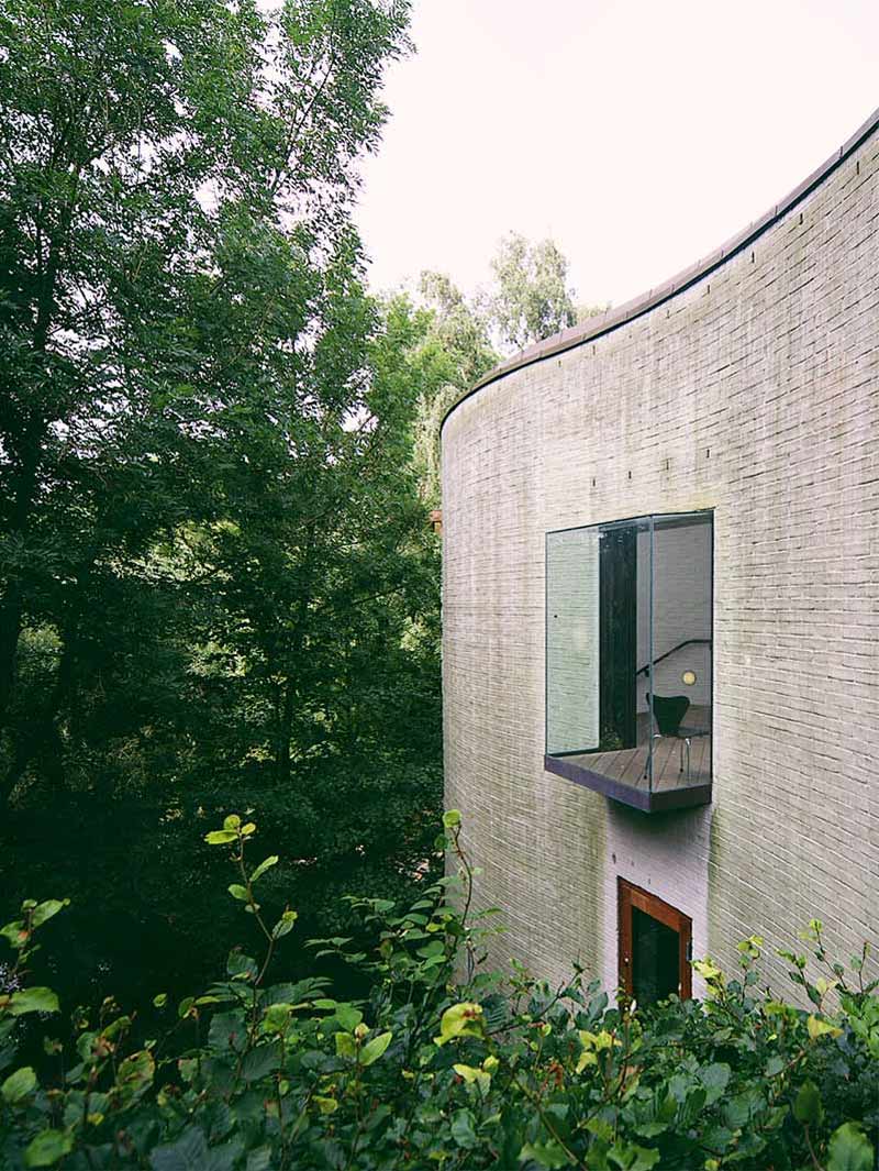Contemporary residential building with a curved brick exterior and small balcony overlooking lush greenery.