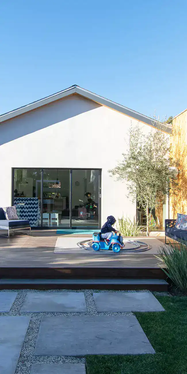 Modern house with a combination of white and wooden exterior walls, large glass sliding doors, and a spacious wooden deck.
