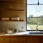 Sunlit laundry room with oak cabinetry, marble countertops, and a large window overlooking a landscaped yard